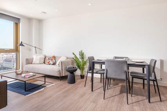 A modern living room with a grey sofa, a glass coffee table, and a dining table with grey chairs.