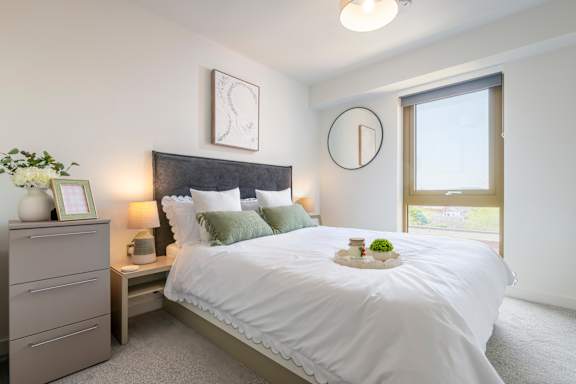 A bedroom with a large bed, a nightstand with a plant, and a clock on the wall.