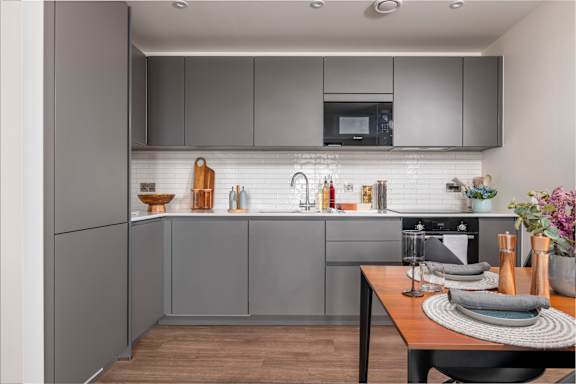 A modern kitchen with grey cabinets and a wooden table set for two.