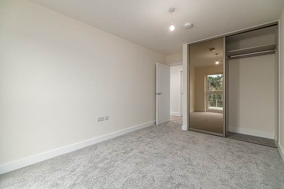 A room with a grey carpet and a sliding door leading to a balcony.