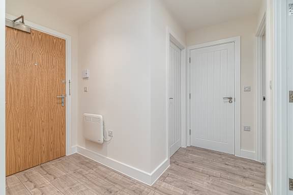 A room with a wooden door and a white wall with a heater.