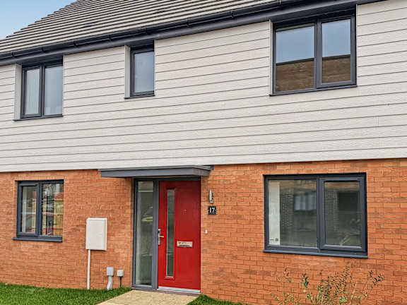 A red door is on the right side of a house with a grey roof.