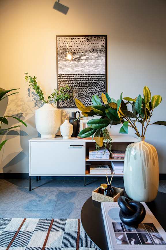 A white cabinet with a vase on top of a coffee table with a plant in it.