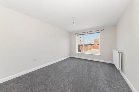 A room with a grey carpet and a window showing a building outside at Origins Apartments, Cambridge, CB3 0UX