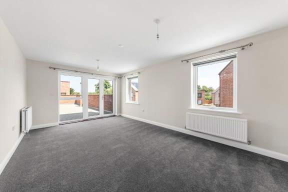 A room with a grey carpet and a window showing a brick building outside at Origins Apartments, Cambridge