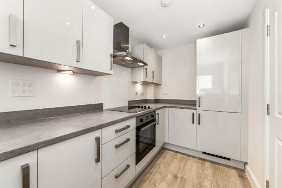 A modern kitchen with white cabinets and a wooden floor at Origins Apartments, Cambridge, CB3 0UX