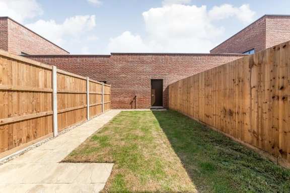 A long, narrow courtyard with brick walls and wooden fences at Origins Apartments, Cambridge, CB3 0UX