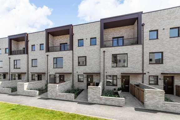 A row of modern apartment buildings with balconies and doors at Origins Apartments, Cambridge