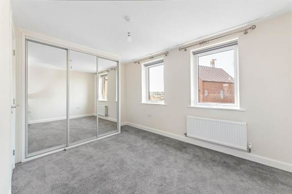A room with a grey carpet and a window showing a red brick house outside at Origins Apartments, Cambridge