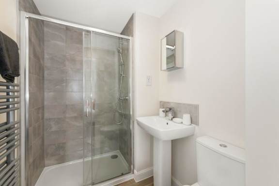 A white sink is on a stand in a bathroom with a glass shower door at Origins Apartments, Cambridge
