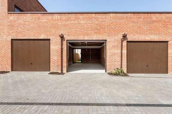 A red brick building with two brown garage doors and a brick walkway leading to a white door at Origins Apartments, Cambridge