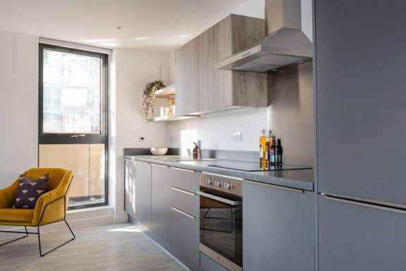 a kitchen with gray cabinets and a yellow chair a kitchen with gray cabinets and a yellow chair at Vox Apartments, Manchester