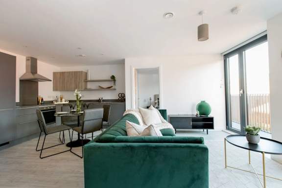 a living room with a green couch and a kitchen with a table and chairs a living room with a green couch and a kitchen with a table and chairs at Vox Apartments, Manchester