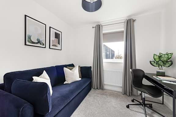 A blue couch with white pillows sits in a room with a desk and chair at The Woodlands Apartments, Milton Keynes, MK5 6GS