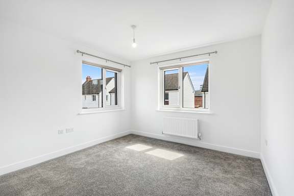 A room with a grey carpet and two windows.