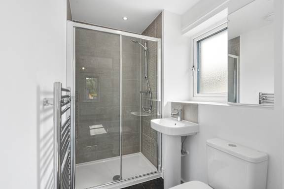 A white sink is in a small bathroom with a walk-in shower.