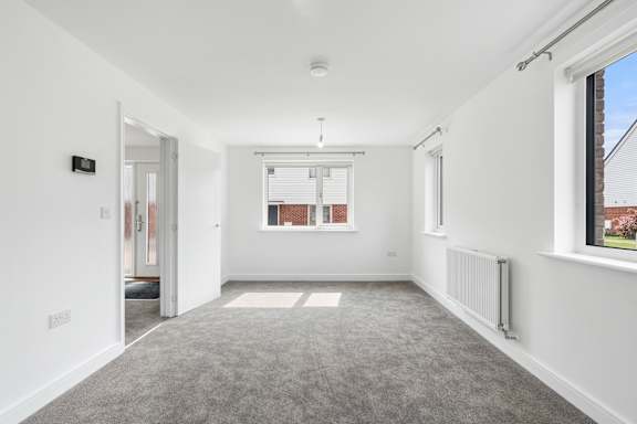 A spacious room with white walls and a grey carpet.