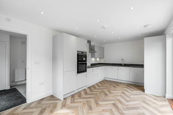 A modern kitchen with a wooden floor and white cabinets.