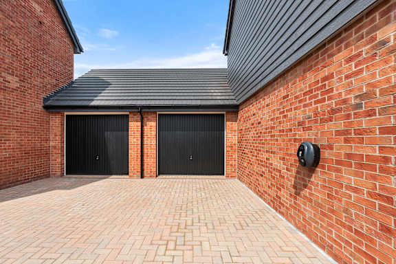 A brick wall with a black garage door and a black vent.