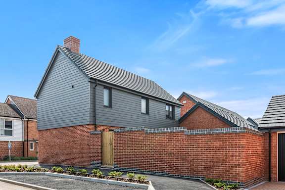 A grey house with a brick wall and a black door.