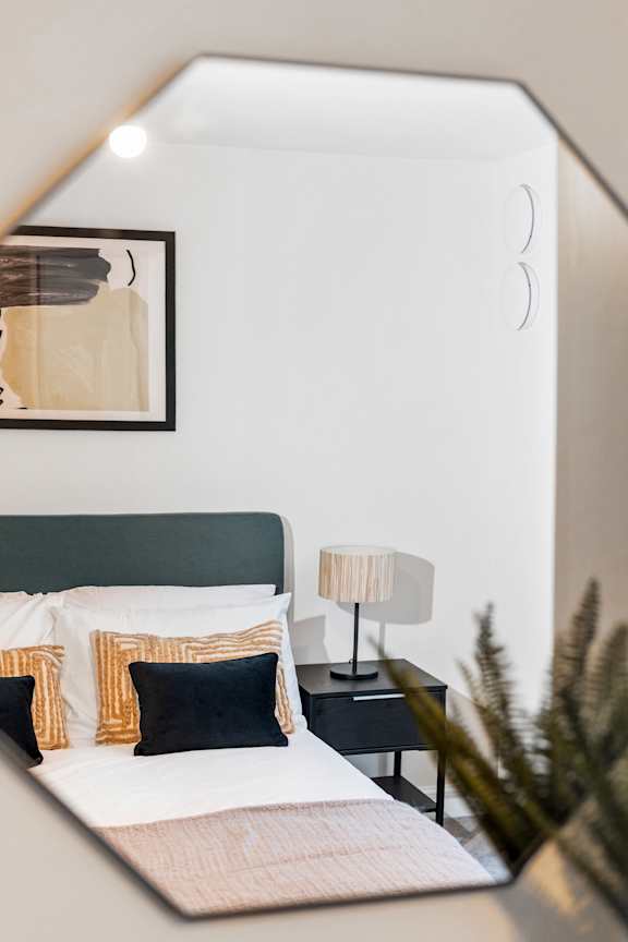 A bed with a white comforter and a green headboard with a lamp and a plant on the nightstand.