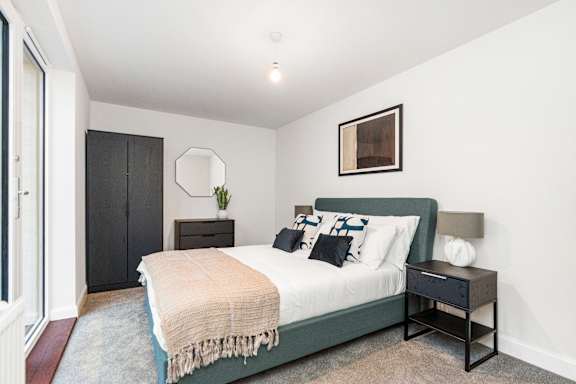 A bedroom with a bed, nightstand, and a plant.