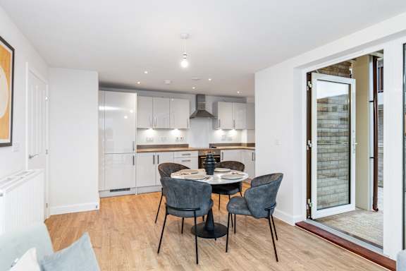 A dining area with a table and chairs in the foreground and a kitchen in the background.