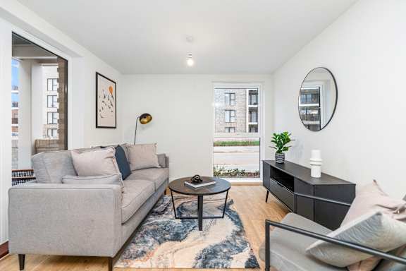 A living room with a grey couch, a black coffee table, and a round mirror on the wall.