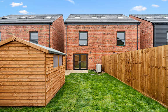 A wooden shed sits in front of a brick house.