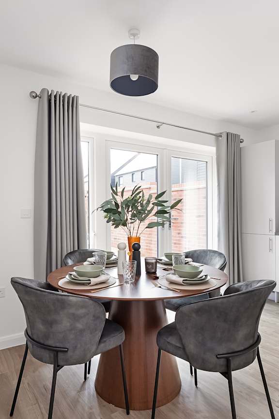 A dining table with chairs and a vase of flowers on it at The Woodlands Apartments, Milton Keynes