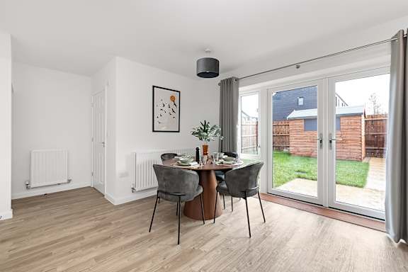 A dining room with a table set for two and a view of a backyard at The Woodlands Apartments, Milton Keynes