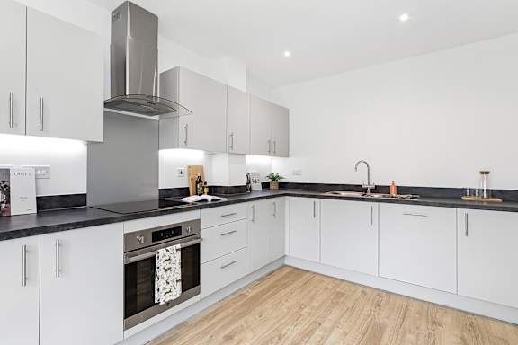 A modern kitchen with white cabinets and a black countertop at The Woodlands Apartments, Milton Keynes, MK5 6GS