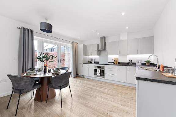 A modern kitchen with a dining table set for two at The Woodlands Apartments, Milton Keynes, MK5 6GS