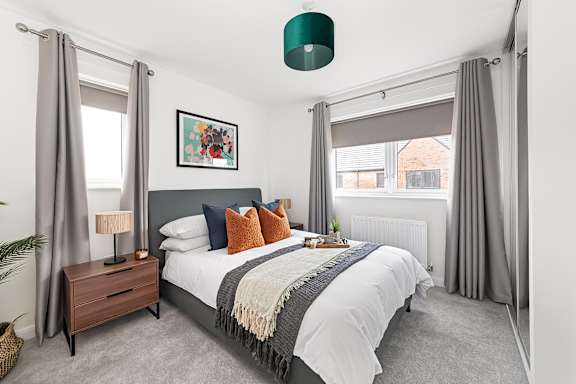 A bedroom with a large bed, a nightstand with a lamp, and a framed picture on the wall at The Woodlands Apartments, Milton Keynes, MK5 6GS