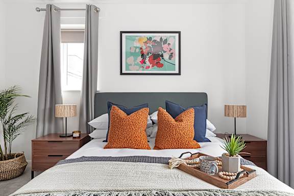 A bedroom with a bed, two lamps, a plant, and a painting on the wall at The Woodlands Apartments, Milton Keynes