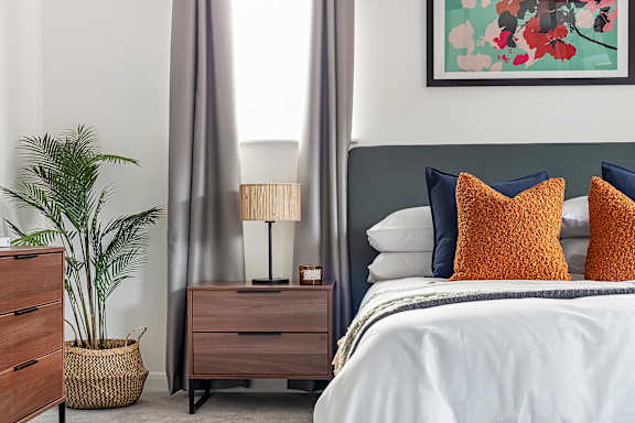 A bedroom with a bed, nightstand, and a plant at The Woodlands Apartments, Milton Keynes