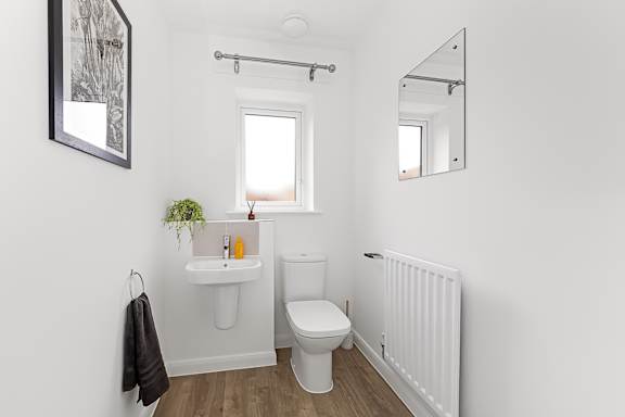 A white bathroom with a toilet, sink, mirror and a window at The Woodlands Apartments, Milton Keynes