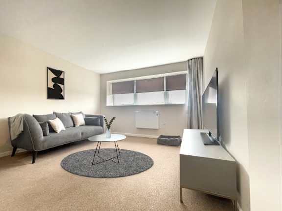 A living room with a grey couch, a white coffee table, a grey ottoman, a flat screen TV, and a window with curtains.
