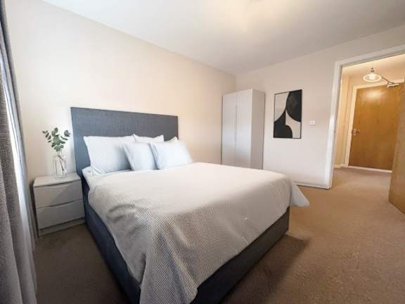 A bedroom with a large bed and a nightstand with a plant on it.
