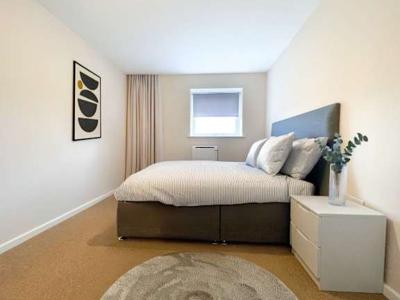 A bedroom with a bed, nightstand, and a framed picture on the wall.