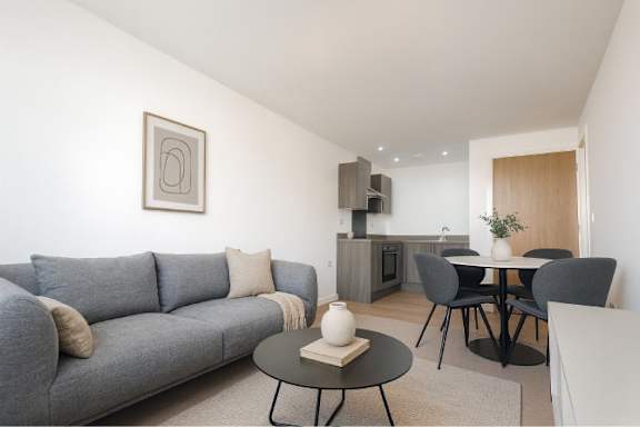 A grey couch with a white pillow sits in a living room with a black coffee table in front of it.
