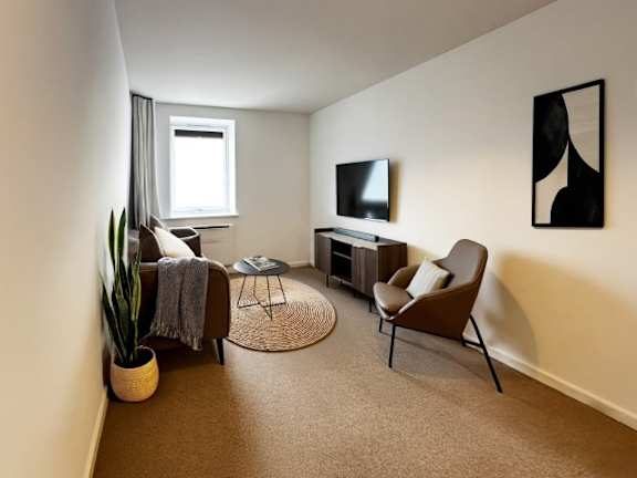 A living room with a brown chair, a grey sofa, a small table, a television, and a potted plant.
