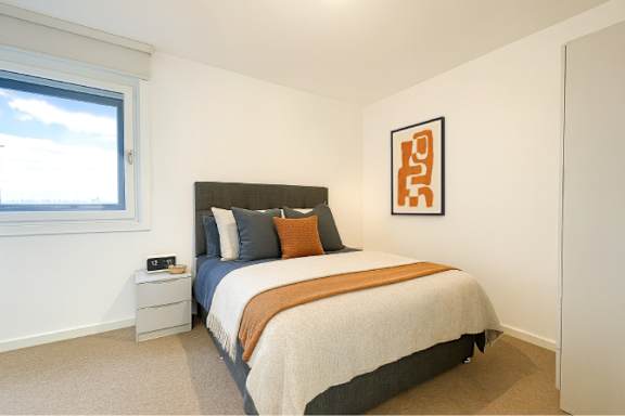 A bedroom with a bed, nightstand, and a window.