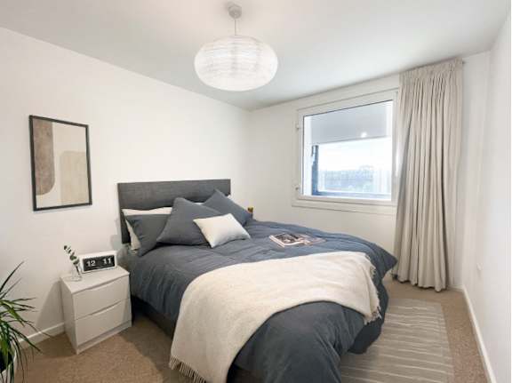 A bedroom with a bed, nightstand, and window.