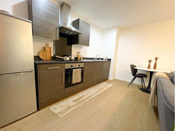 A modern kitchen with a refrigerator, oven, and a dining area with a chair and table.
