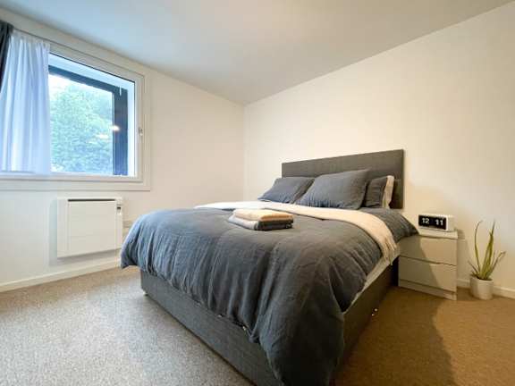 A bedroom with a bed, nightstand, and window.