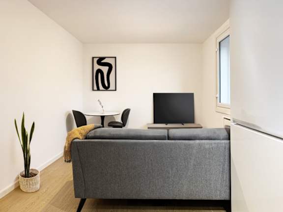 A grey bed with a black screen and a white table with a black object on it.