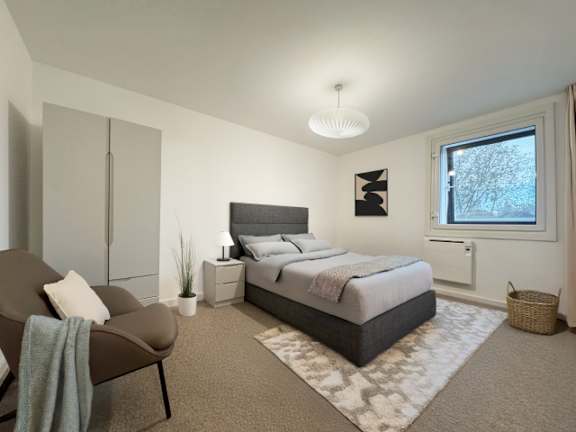 A bedroom with a large bed, a chair, and a window.