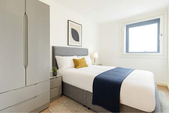 A bedroom with a bed, nightstand, and a grey headboard.