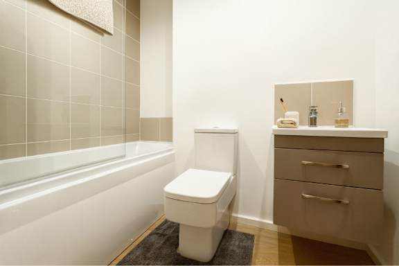 A white toilet sits in a bathroom next to a bathtub and a vanity with drawers.